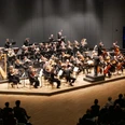 Orchester Osnabrücker Musikfreunde Orchester spielt auf einer Bühne, Musiker in formeller Kleidung konzentrieren sich auf Instrumente.