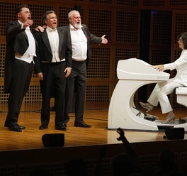 luciano_presse.jpg Drei Männer in Anzug halten sich singend neben einem weißen Klavier im Arm