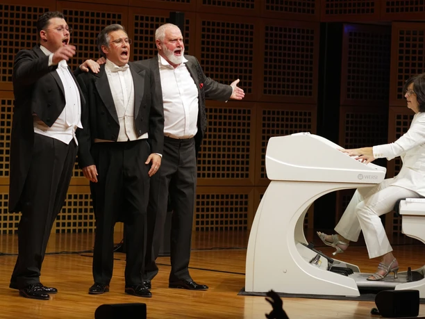 luciano_presse.jpg Drei Männer in Anzug halten sich singend neben einem weißen Klavier im Arm