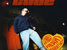 Ein junger Mann steht leicht gebeugt mit einem Kapuzenpullover und Baseballkappe in einer dunklen Umgebung.