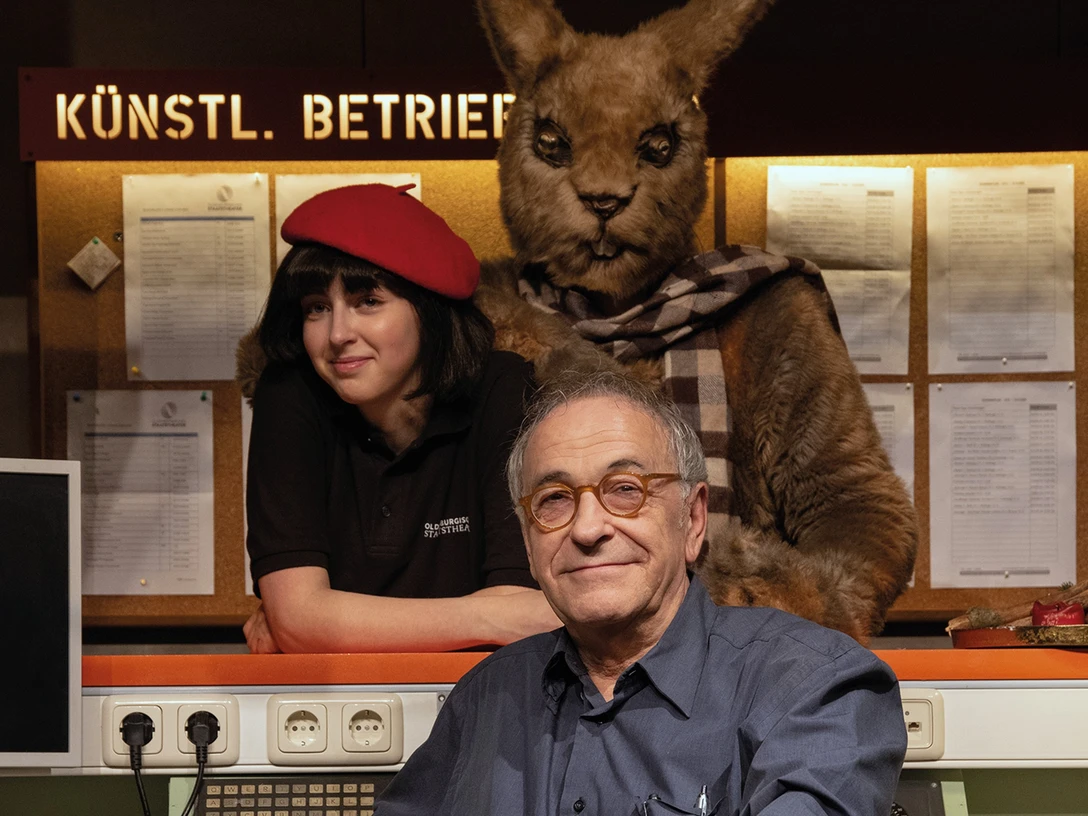 theater-laboratorium-c-theater-laboratorium-quer-cmyk-2.jpg Drei Personen in einem Theaterbüro, darunter eine Person im Känguru-Kostüm, freundlich lächelnd.