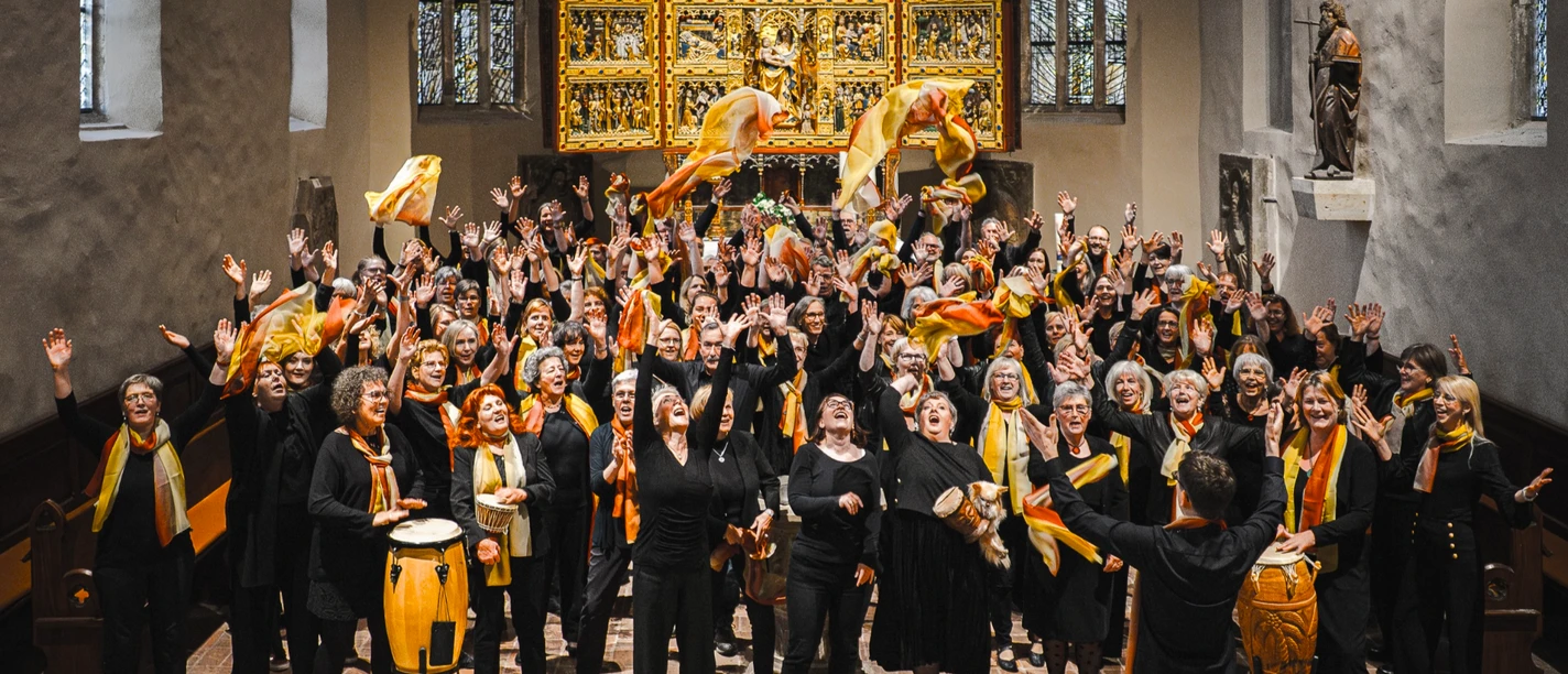 HWO2025 Gospelchor in der Kirche mit erhobenen Händen und bunten Tüchern vor goldenem Altar.