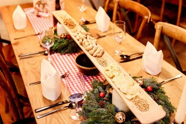 Een feestelijk gedekte tafel met lange houten planken vol hapjes, omringd door kerstversieringen.