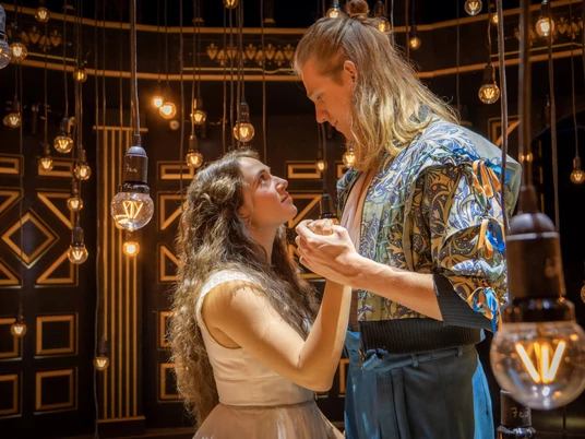 Romeo & Julia Zwei Schauspieler während einer Aufführung von Romeo und Julia in einer intimen Szene. Sie stehen unter warm leuchtendem Licht, das eine romantische und fesselnde Atmosphäre schafft.Two actors during a performance of Romeo and Juliet in an intimate scene. They stand under a warm glow of light that creates a romantic and captivating atmosphere.