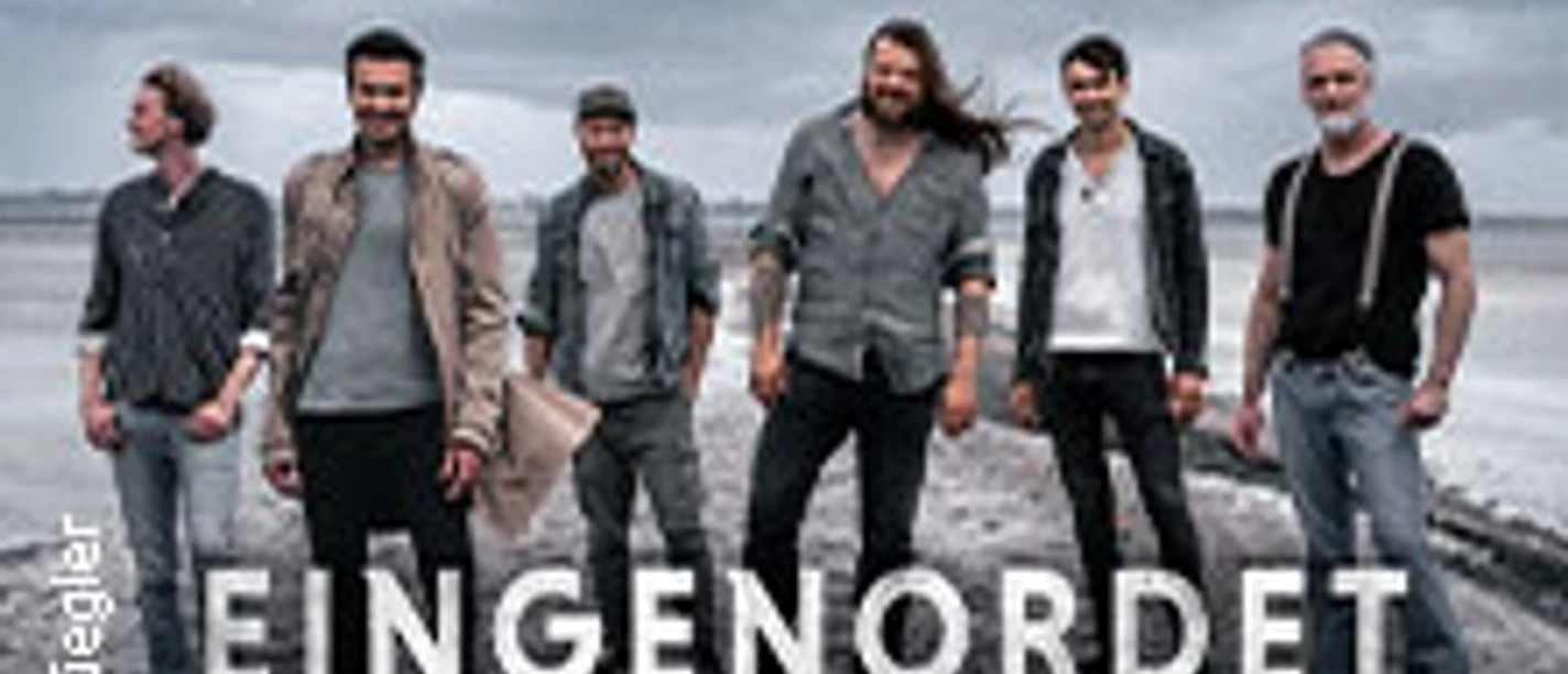 Sechs Bandmitglieder von Versengold stehen entschlossen am Strand, im Hintergrund das Meer.