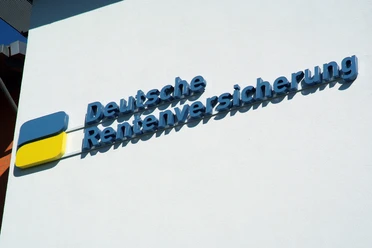 foto_logo_schriftzug.jpg Das Bild zeigt ein blau-gelbes Logo mit dem Schriftzug "Deutsche Rentenversicherung" an einer weißen Wand.
