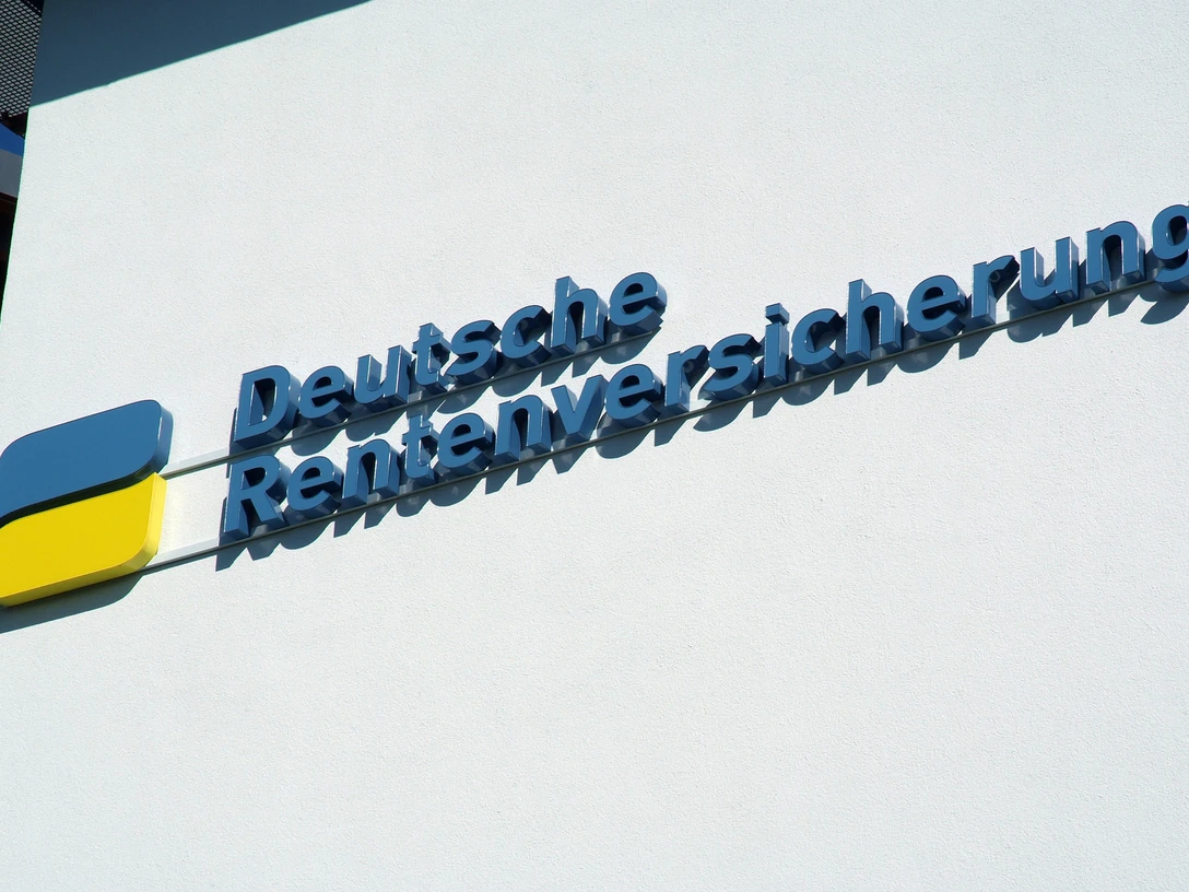 foto_logo_schriftzug.jpg Das Bild zeigt ein blau-gelbes Logo mit dem Schriftzug "Deutsche Rentenversicherung" an einer weißen Wand.