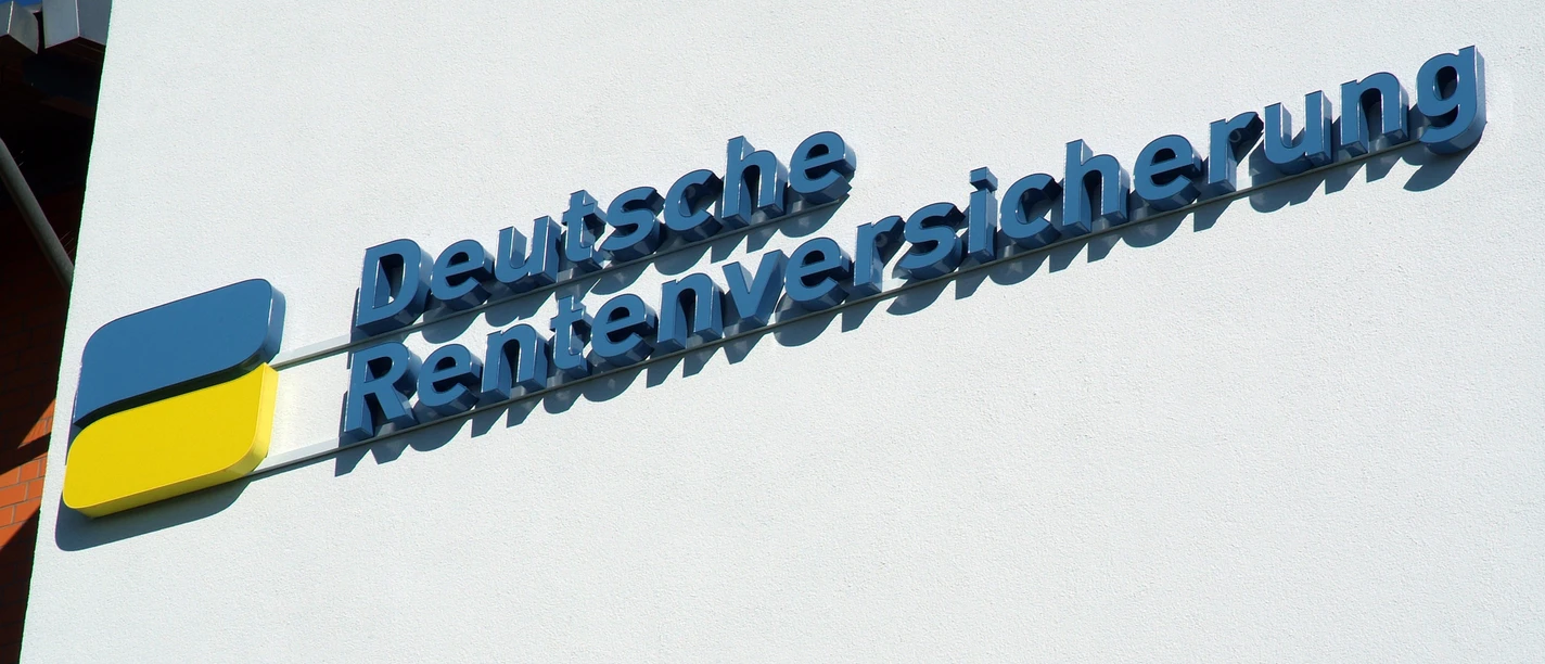 foto_logo_schriftzug.jpg Das Bild zeigt ein blau-gelbes Logo mit dem Schriftzug "Deutsche Rentenversicherung" an einer weißen Wand.