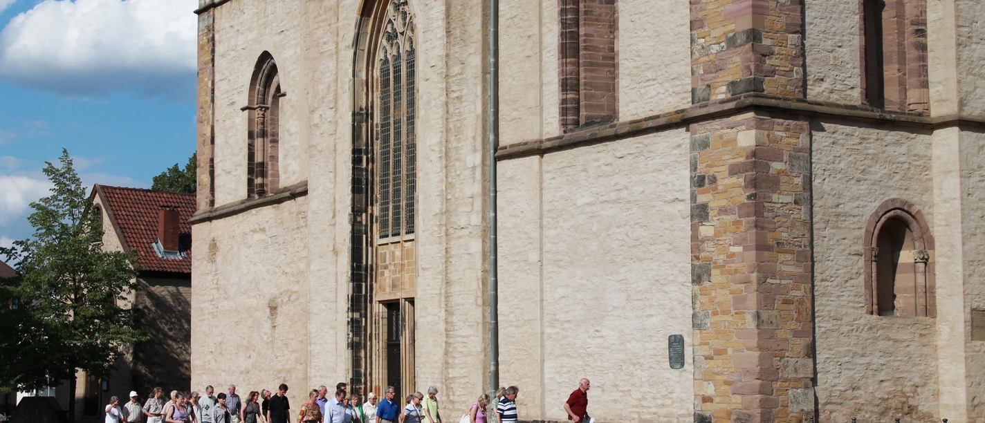 Eine Gruppe von Menschen besichtigt das beeindruckende historische Münster vor sonnigem Himmel.