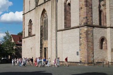 stadtf-hrung_vor_m-nster_feg Eine Gruppe von Menschen besichtigt das beeindruckende historische Münster vor sonnigem Himmel.