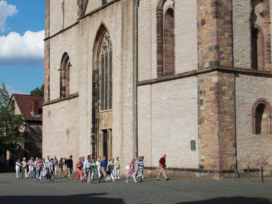 stadtf-hrung_vor_m-nster_feg Eine Gruppe von Menschen besichtigt das beeindruckende historische Münster vor sonnigem Himmel.