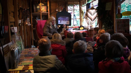 Eine Frau liest einer Gruppe von Kindern in einer hölzernen Hütte auf dem Weihnachtsmarkt vor.
