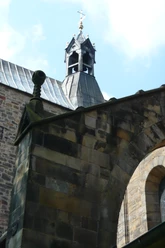 6 Stiftskirche.JPG Glockenturm der Stiftskirche mit steinernem Bogen und mittelalterlichem Mauerwerk unter blauem Himmel.