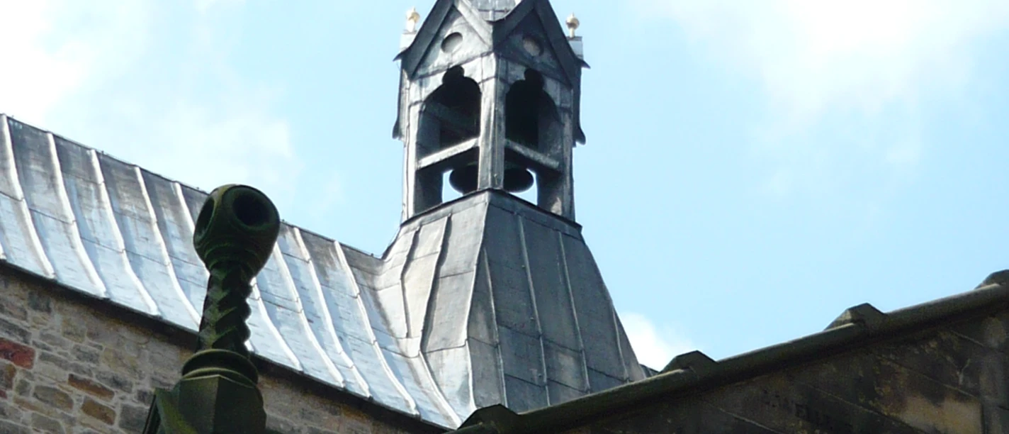 6 Stiftskirche.JPG Glockenturm der Stiftskirche mit steinernem Bogen und mittelalterlichem Mauerwerk unter blauem Himmel.