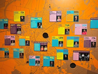 Geschichten-des-Ankommens.jpg Verschiedene bunte Tafeln mit Porträts von Menschen und deren Herkunftsländern.