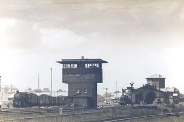 Bahnhof Wunstorf Stellwerk.jpg Historisches Stellwerk in Wunstorf mit umliegenden Gleisen und einer Dampflok bei Tageslicht.