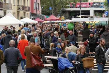 Block Party On a busy street, many people gather at a street party with colorful stalls.