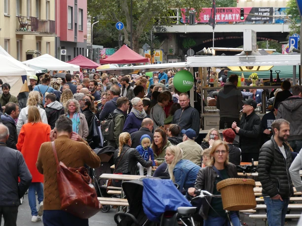 Block Party On a busy street, many people gather at a street party with colorful stalls.