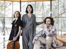 Drei Musiker, ein Cello, eine helle Treppe mit Glasscheiben, stilvoll gekleidet in einem modernen Raum.