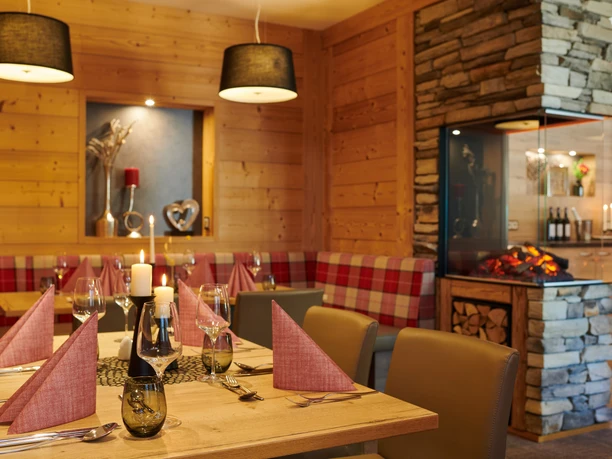 Cozy restaurant with wooden interior, table setting, fireplace and modern lighting.