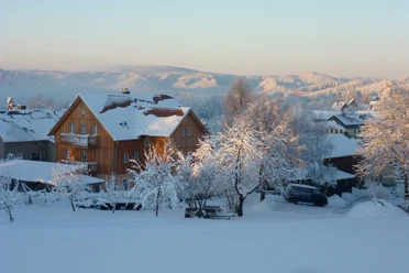 Vakantiehuis in een besneeuwd winterlandschap op een heldere dag, omringd door besneeuwde bomen.