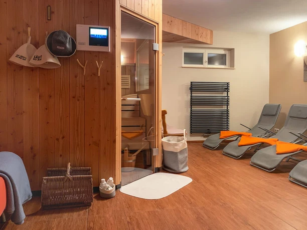 Sauna Ferienhaus Winterbergblick Saunaraum mit Holzverkleidung: Liegestühle mit orangenen Decken, links Holztür zur Sauna, helle Beleuchtung.