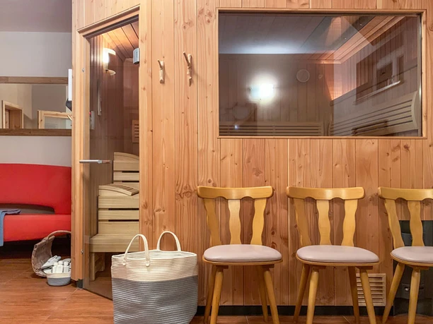 Sauna Außenbereich Ferienhaus Winterbergblick Sauna mit Holzwänden, drei Stühlen und großem Fenster im Ferienhaus nahe Winterbergblick.