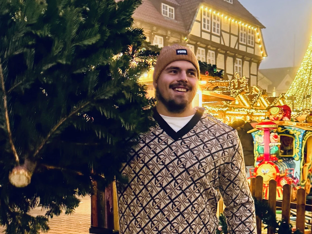 Der Gewinner von 2024: Max Dehning Max Dehning mit festlichem Hintergrund auf Weihnachtsmarkt, lächelnd mit Tanne.Max Dehning with festive background at Christmas market, smiling with fir tree.Max Dehning med festlig baggrund på julemarked, smilende med grantræ.Max Dehning met feestelijke achtergrond op kerstmarkt, lachend met dennenboom.