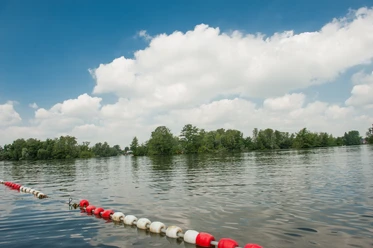 Badestelle am Prüßsee Sanftes Wasser mit grüner Insel, bewölkter Himmel darüber. Uferabsperrung mit rot-weißen Bojen.