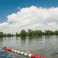 Badestelle am Prüßsee Sanftes Wasser mit grüner Insel, bewölkter Himmel darüber. Uferabsperrung mit rot-weißen Bojen.