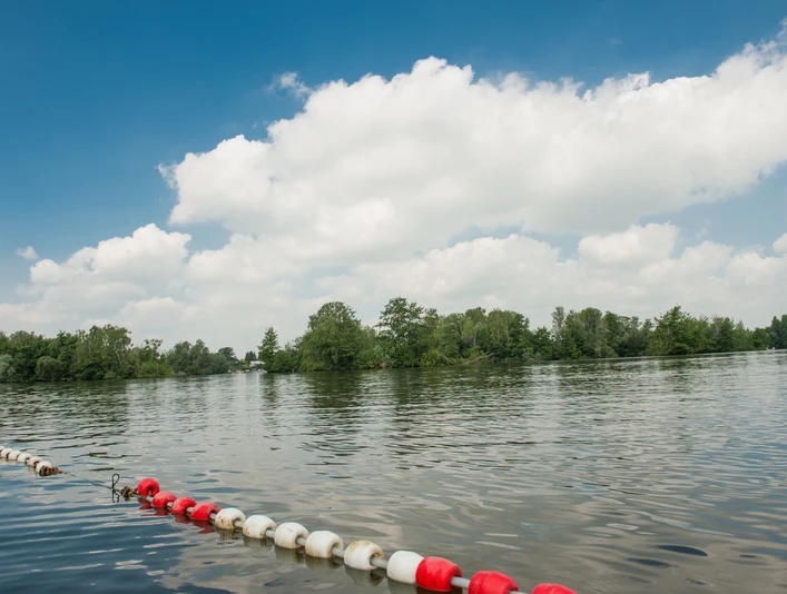 Badestelle am Prüßsee Sanftes Wasser mit grüner Insel, bewölkter Himmel darüber. Uferabsperrung mit rot-weißen Bojen.