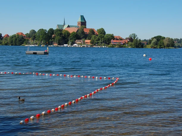 Blick auf Dominsel_ Badestelle Bäk Blick auf den Ratzeburger See mit roten Bojen im Vordergrund und Ratzeburg mit Dom im Hintergrund.