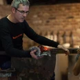Erwachsenen Kurs.jpg Ein Glasbläser konzentriert sich auf die Formung einer glühenden Glasmasse in einer Werkstatt.