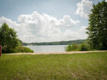 Bademöglichkeit Rolandseck Der Lütauer See in Mölln mit grünem Ufer und Bäumen unter einem bewölkten Himmel.