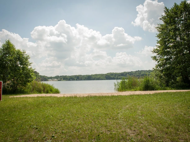 Bademöglichkeit Rolandseck Der Lütauer See in Mölln mit grünem Ufer und Bäumen unter einem bewölkten Himmel.