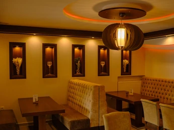 erlebniscard-suvai-kitchen (1).jpg Warmes Licht beleuchtet stilvolles Restaurantinterieur mit eleganten Holzmöbeln und gepolsterten Bänken.