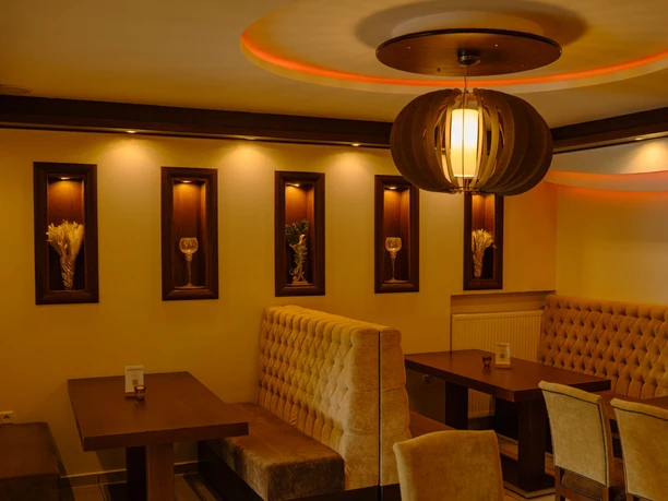 erlebniscard-suvai-kitchen (1).jpg Warmes Licht beleuchtet stilvolles Restaurantinterieur mit eleganten Holzmöbeln und gepolsterten Bänken.