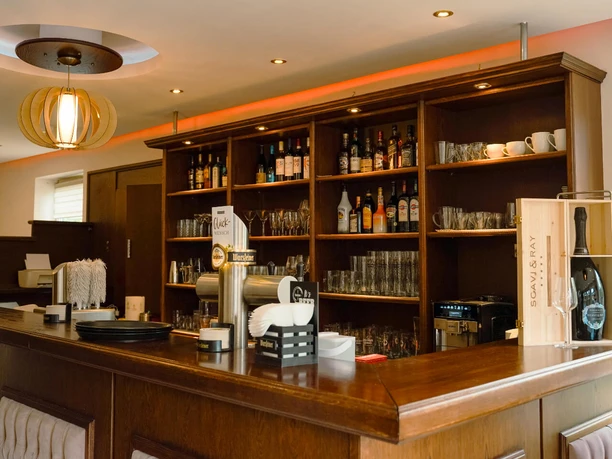 bad-fallingbostel-suvai-kitchen-erlebniscard (1).jpg Barbereich mit hölzerner Theke, Regalen voller Gläser und einladender Beleuchtung.