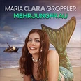 Maria Clara Groppler als Meerjungfrau mit grünem Fischschwanz sitzend vor einem sonnigen Strand.