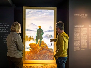 CDFRIEDRICHINSPIRIERT Zwei Besucher betrachten ein digitales Gemälde von Caspar David Friedrich. Two visitors look at a digital painting by Caspar David Friedrich.Dva návštěvníci si prohlížejí digitální obraz Caspara Davida Friedricha.Twee bezoekers bekijken een digitaal schilderij van Caspar David Friedrich.Dwóch odwiedzających przygląda się cyfrowemu obrazowi Caspara Davida Friedricha.Due visitatori osservano un dipinto digitale di Caspar David Friedrich.