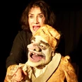 ambrella-figurentheater-der-eingebildete-kranke-1.jpg Frau spielt mit lebendiger Puppe in goldener Kleidung eine Theaterszene voller Ausdruckskraft.