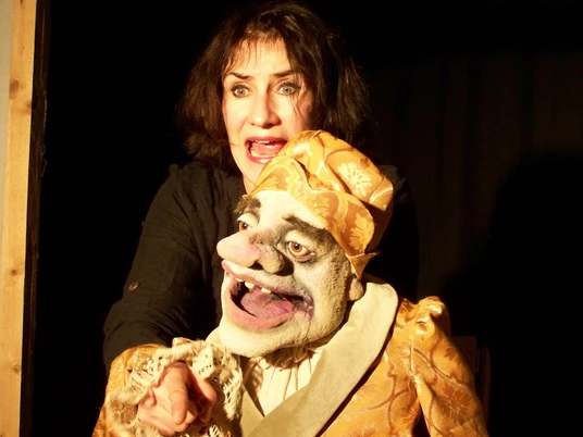 ambrella-figurentheater-der-eingebildete-kranke-1.jpg Frau spielt mit lebendiger Puppe in goldener Kleidung eine Theaterszene voller Ausdruckskraft.
