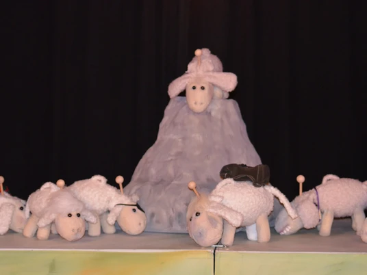 figurentheater-grinsekatze-das-letzte-schaf-2.jpg Mehrere weiße Schafpuppen stehen auf einer Bühne, eines thront erhöht auf einem grauen Hügel.