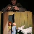 ambrella-figurentheater-zottelhaube-1.jpg Puppenspielerin lenkt Marionetten von zwei Kindern und einer Ziege in einer Holzkulisse.