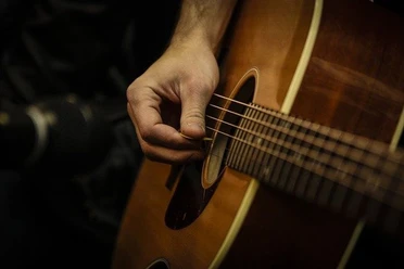 Live Musik Nahaufnahme einer Hand, die mit einem Plektrum eine Akustikgitarre anschlägt, Musikstimmung live.
