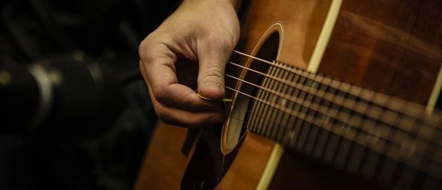 Live Musik Nahaufnahme einer Hand, die mit einem Plektrum eine Akustikgitarre anschlägt, Musikstimmung live.