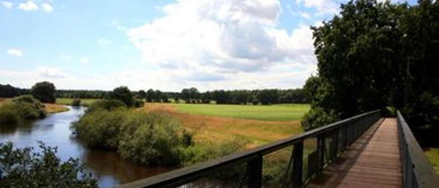 Holzbrücke über die Hase mit Blick auf Flusslandschaft, grüne Wiesen und blauen Himmel mit Wolken