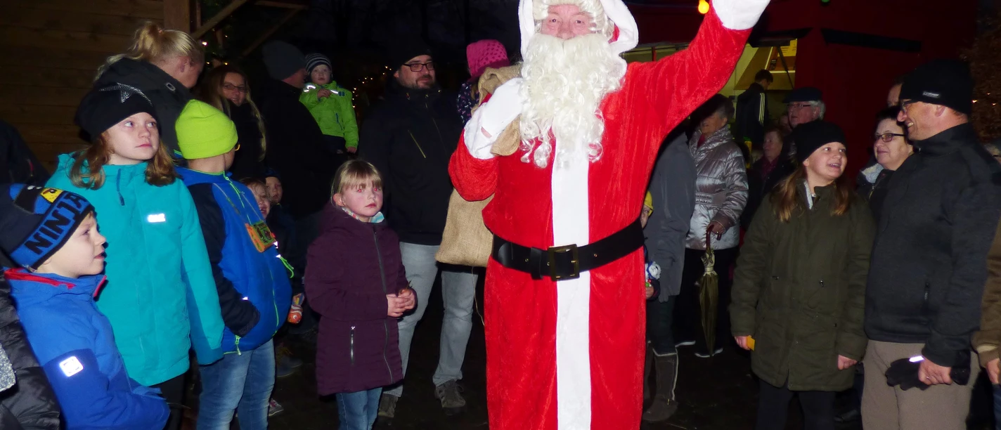 Sinterklaas zwaait op de Sinterklaasmarkt, omringd door kinderen en bezoekers.