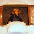 figurentheater-ernst-heiter-frau-holle.jpg Holzfigur der Frau Holle steht am Fenster und schüttelt ein weiß besticktes Kissen aus.