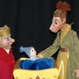 annes-buehne-der-prinz-mit-den-eselsohren-1.jpg Figurenpuppen eines Königs, einer Königin und eines Babys in Wiege vor dunklem Hintergrund